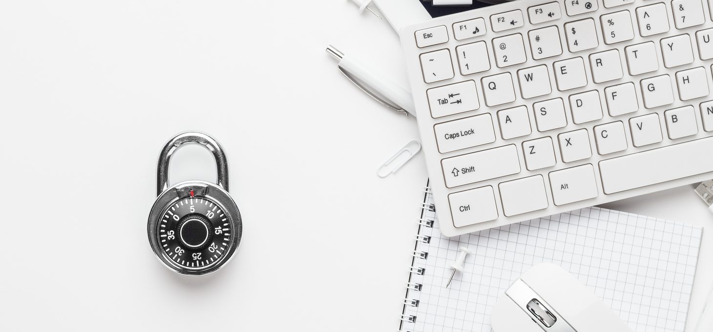 Lock with a dial next to a keyboard, opened notebook, pens, and other office supplies